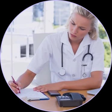 Clinician with a stethoscope writing notes at a desk