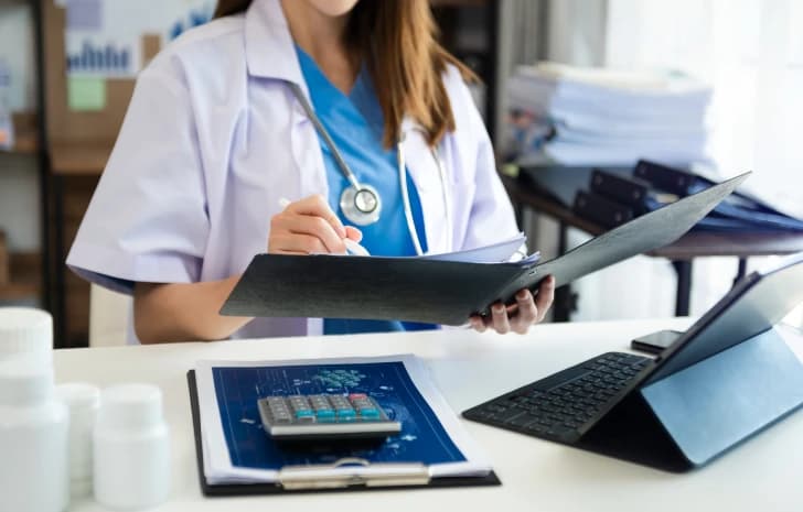 Clinician reviewing a billing folder at a desk with a tablet and calculator