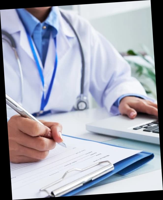 Orthopedic physician writing on a claim form beside a laptop