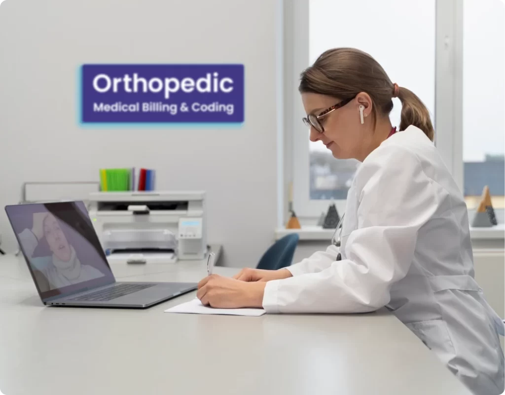 Orthopedic billing and coding specialist writing notes at a desk beside a telehealth call, under an Orthopedic Medical Billing & Coding office sign