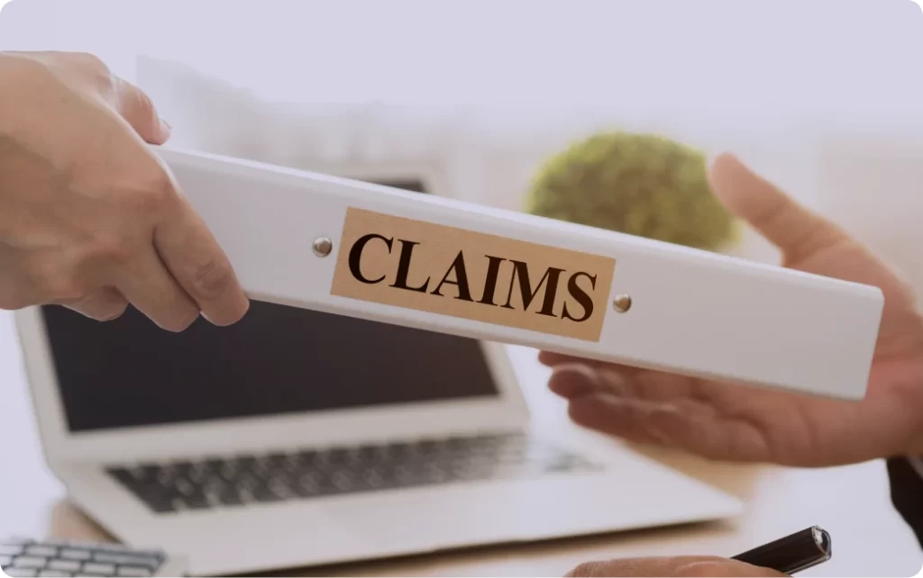 Hands passing a binder labeled Claims across a desk