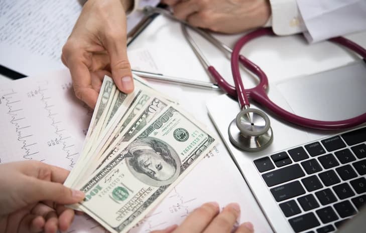 Patient handing cash payment to a doctor at a laptop