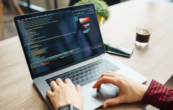 Person coding on a laptop at a wooden desk